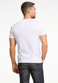 T-shirt bianco in cotone con colletto a girocollo, maniche corte e design semplice, abbinato a jeans in denim scuro con tasche posteriori e cuciture arancioni.
