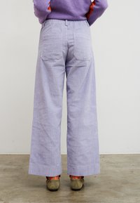 Φαρδιά παντελόνια κορδούρας σε ανοιχτό λεβάντα, με κάθετες ραβδώσεις, δύο πίσω τσέπες και τελείωμα που φτάνει λίγο πάνω από τα παπούτσια.