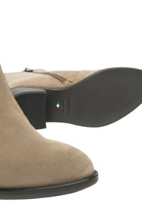 Beige suède enkellaarzen met een ronde neus, een ritssluiting aan de zijkant en een lage blokhak. De zool is zwart rubber met horizontale groefpatronen.