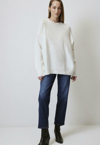 Oversized white knit sweater with ribbed hem and cuffs, paired with dark blue straight-leg jeans and black heeled ankle boots.