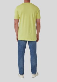 HeldGeel T-shirt met korte mouwen en een klassieke ronde hals, gecombineerd met blauwe denim jeans en witte sneakers. Eenvoudig ontwerp, minimale details.