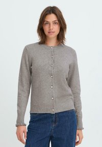 Cardigan en tricot gris avec un col rond, des boutons sur le devant et des poignets volantés. Le tissu a une texture douce et un design ajusté.