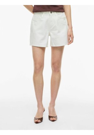 Person iført hvide denims-shorts kombineret med brune åbne hæle og en marsala top, der er stoppet ind, vist fra talje til fødder.