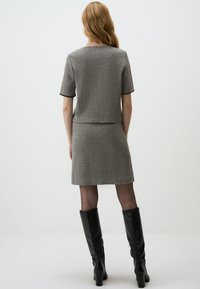Ensemble gris en deux pièces comprenant un haut ajusté et une jupe, en tissu texturé, avec des manches courtes et des bords ourlés, associé à des bottes noires montantes.