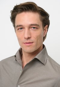 Camisa de color gris claro, con cuello y una textura suave. Botones visibles y un cuello ligeramente abierto. Figura masculina con cabello corto y estilizado.