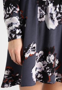 Robe fluide en tissu doux, présentant une base gris foncé ornée de grands motifs floraux blancs et rouges. Avec des manches longues et une coupe ample.