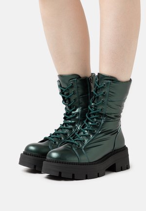 Bottes vert métallisé à lacets avec un haut rembourré, une semelle en caoutchouc noire épaisse et des détails de couture visibles pour une texture supplémentaire.