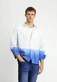 Wit en blauw verloop overhemd met knopen. Gepresenteerd in een gestructureerde stof met opgerolde mouwen. Gecombineerd met donkerblauwe denim jeans.