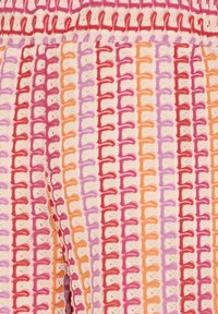 Gros plan sur un tissu tissé avec des rayures verticales rouges, roses, oranges et violettes, présentant des motifs de points en boucle sur un fond clair.