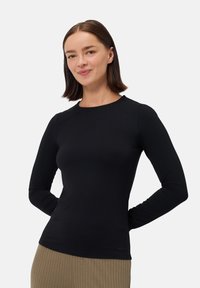 Černý top s dlouhými rukávy a kulatým výstřihem, hladká textura, přiléhavý střih a žádné viditelné vzory nebo přijímací prvky. Nosený s béžovými žebrovanými kalhotami.