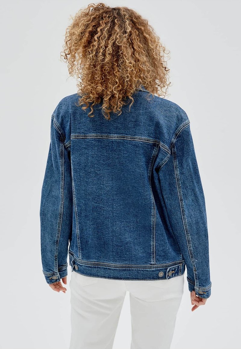 Giacca di denim blu con un design classico, caratterizzata da una vestibilità leggermente ampia, cuciture in evidenza e dettagli in metallo sui polsini e sull'orlo.