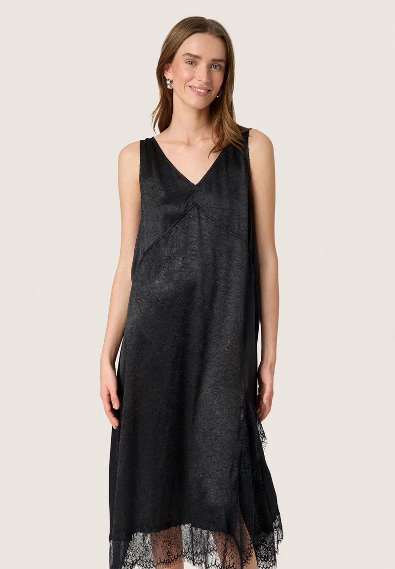 Schwarzes ärmelloses Kleid aus strukturiertem Stoff, mit V-Ausschnitt, asymmetrischem Saum und Spitzenakzenten entlang des unteren Randes.