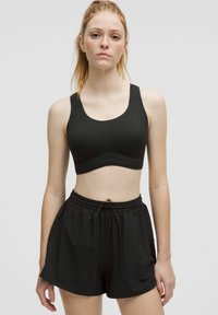 Black sports bra with a rounded neckline, wide straps, and a smooth texture, paired with black athletic shorts featuring an elastic waistband.