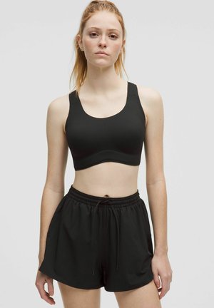 Black sports bra with a rounded neckline, wide straps, and a smooth texture, paired with black athletic shorts featuring an elastic waistband.