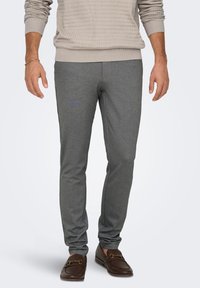 Pantalon gris en tissu doux avec une coupe slim, présentant une texture lisse et une ceinture élastique, associé à des mocassins marron foncé.
