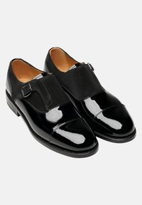Schwarze Lederschuhe mit patentiertem Finish, einem Monk-Strap mit Schnalle und einer glatten Oberfläche. Abgerundete Zehenpartie mit kontrastierenden Texturen.