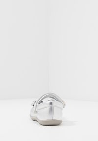 Ballet flat argenté avec une finition métallique, sangle ajustable et bout arrondi. Semelle douce avec un profil minimal ; design discret.