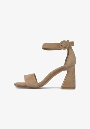 Sandalia de tacón alto de ante beige con un amplio tacón cuadrado, punta abierta y correa ajustable en el tobillo con un hebilla redonda. Textura suave.