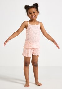 Valkoinen puuvillainen yöasu, jossa on ribbitekniikalla valmistettu toppi ohuilla olkaimilla ja liehukehelmalla, yhdistettynä vastaaviin shortseihin, joita koristavat pienet punaiset yksityiskohdat.