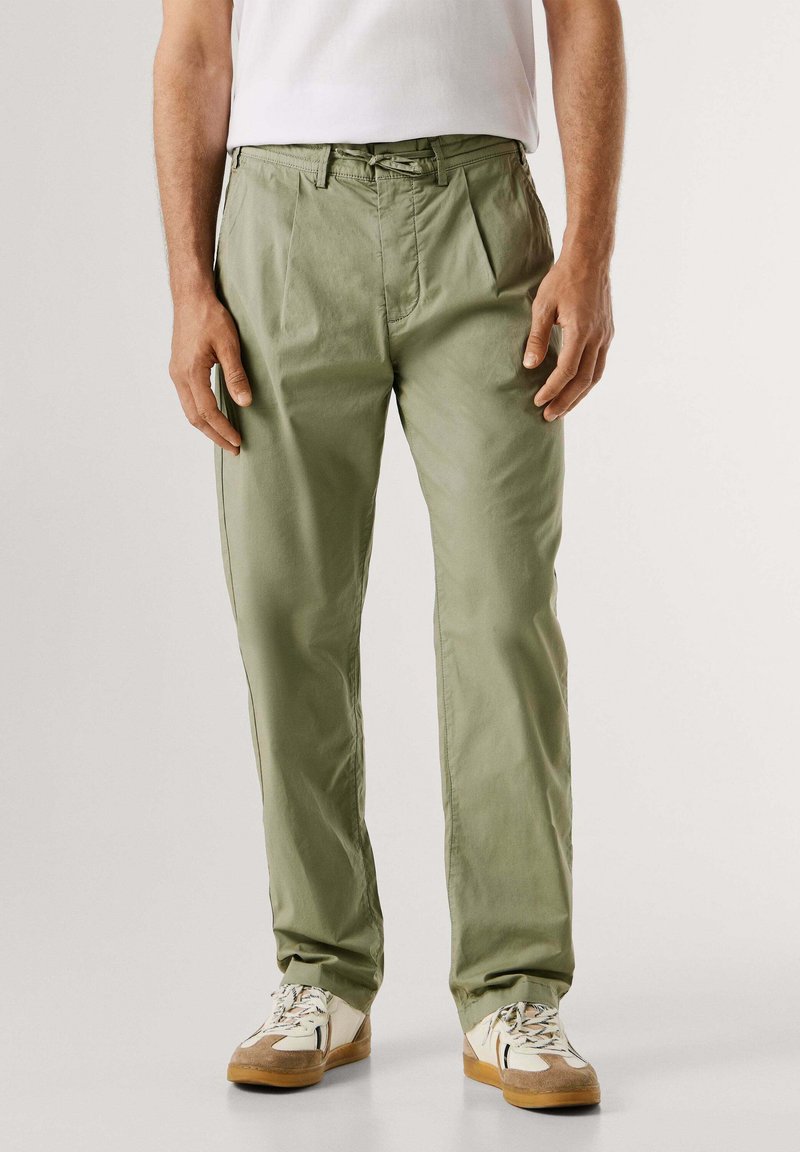 Lichtgroene chino's met een relaxte pasvorm, voorplooien, zijzakken en een gladde textuur. Gecombineerd met beige en witte sneakers.