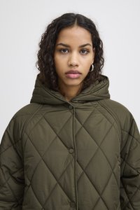 Jachetă căptușită de culoare verde măsliniu, cu glugă, care prezintă un model cu romburi, nasturi tip snap și o croială lejeră. Țesătură netedă și material de greutate medie.