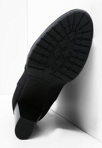 Botín negro con suela de goma texturizada, tacón cuadrado y parte superior lisa. Presenta un diseño de banda de rodadura para tracción y estabilidad.