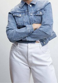 Kurtka dżinsowa w jasnoniebieskim kolorze z zapięciem na guziki z przodu, kieszeniami na piersi i skróconym dołem. Dobrana do białych, wysokowarstwowych spodni. Gładka faktura.