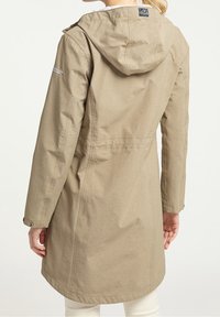 Long manteau beige à capuche, fabriqué en tissu durable. Il présente une taille cintrée, des poches latérales et des détails à boutons sur les manches.
