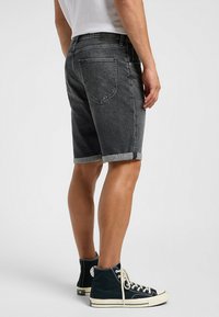 Shorts de mezclilla negra con dobladillos enrollados, que cuentan con un diseño clásico de cinco bolsillos y detalles de costura en la parte trasera. Combinados con zapatillas altas negras.