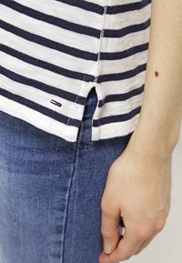 T-paita, jossa on sinivalkoraidat, sivureiät ja pieni logo. Kevyt kangas ja rento leikkaus, yhdistetty tummansinisiin farkkuihin.