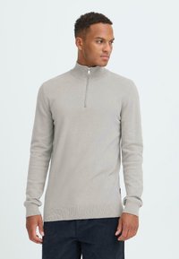 Lys grå zip-neck genser med lange ermer, ribbestrikkede mansjetter og nederkant, myk tekstur, med en kvart lengde glidelås ved halsen.