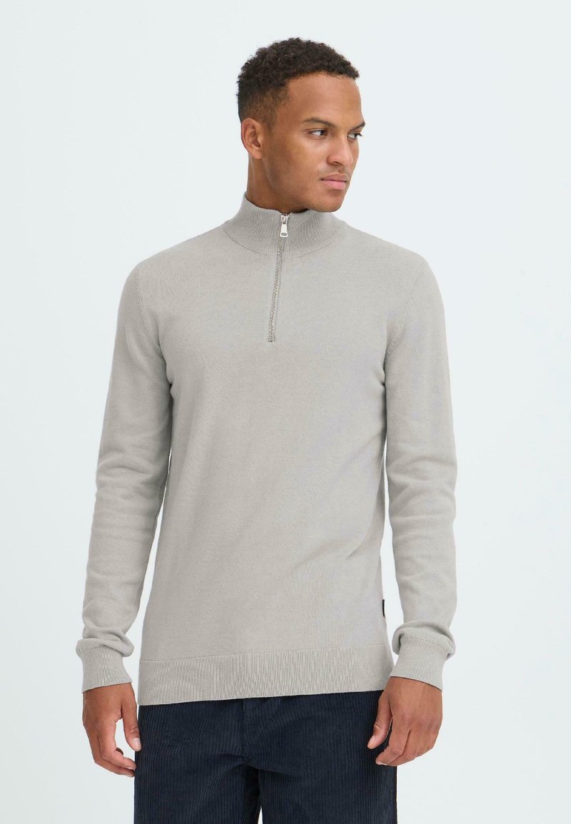 Pullover grigio chiaro con zip a collo alto, maniche lunghe, polsini e orlo a coste, texture morbida, caratterizzato da una zip di un quarto di lunghezza all'apertura del collo.
