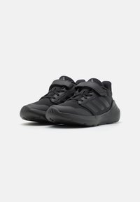 Chaussures de sport noires en mesh respirant, dotées d'une semelle en caoutchouc robuste, d'une sangle Velcro ajustable et de trois bandes latérales distinctes.