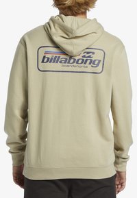 Sudadera color caqui con un gran logo de Billabong en azul marino en la parte posterior, de corte clásico, capucha con cordón y puños y dobladillo acanalados.