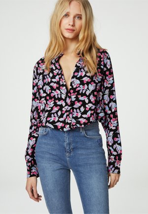 Zwart button-up shirt met bloemenprint, met paarse, roze en witte bloemen. Zachte stof, lange mouwen, gecombineerd met high-waisted blauwe jeans.