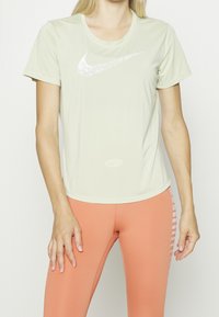 Top deportivo de manga corta en verde claro con un sutil logotipo blanco de Nike en el pecho, combinado con leggings naranja claro que presentan franjas laterales.
