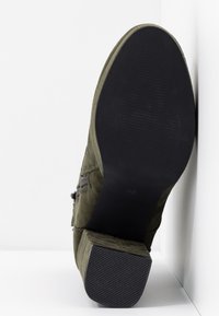 Botte midi en suède olive, présentant une semelle en caoutchouc noir texturé et un talon large, avec un détail de fermeture éclair sur le côté. Indication de taille : 36.