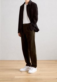 Czarna kurtka z kordurowej tkaniny, biała koszulka, oliwkowe spodnie z kordurowu i białe trampki. Prosty fason z otwartym przodem i bez widocznych wzorów.