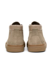 Une paire de sneakers mi-hautes en suède beige avec des cols rembourrés et des semelles en caoutchouc tan, vue de l'arrière sur un fond blanc.