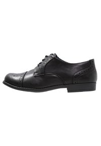 Chaussure Oxford en cuir noir avec détails perforés, bout rond, design à lacets et petit talon pour la stabilité. Texture lisse et silhouette classique.