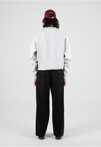Felpa over-size grigia, pantaloni neri a gamba larga e berretto bordeaux. Dettagli notevoli includono polsini a coste e due bottoni decorativi sul retro.