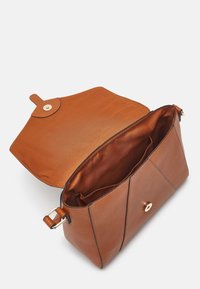 Brązowa skórzana torebka na ramię z otwartą klapą, ukazująca gładkie wnętrze i dwie wewnętrzne kieszonki, ustawiona na białym tle.