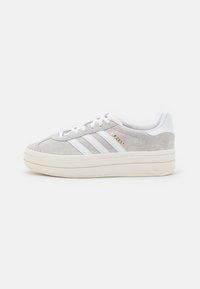 Gray suede sneakers with white leather accents, featuring three white stripes, a thick cream sole, and gold branding detail on the side.
