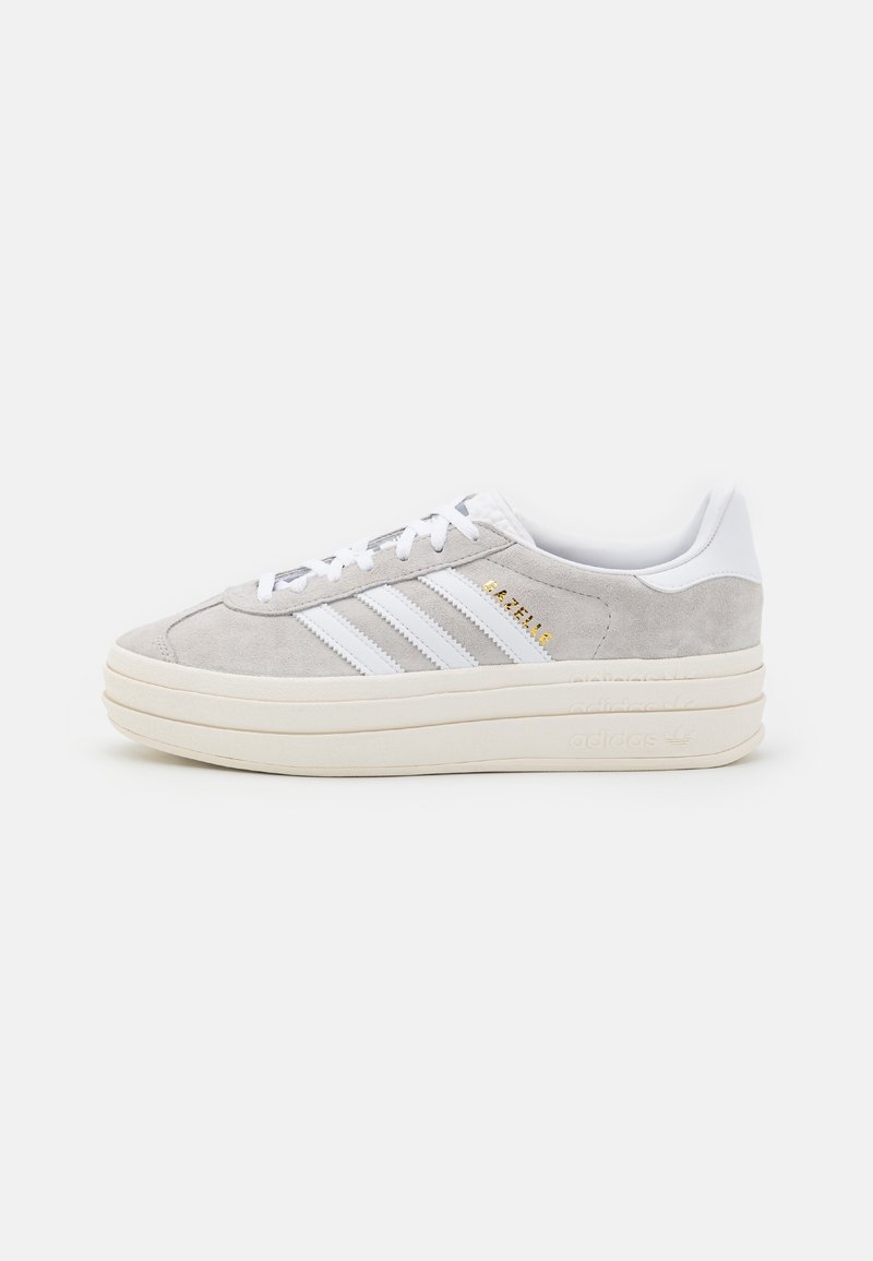 Gray suede sneakers with white leather accents, featuring three white stripes, a thick cream sole, and gold branding detail on the side.