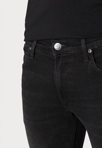 Černé džíny z bavlny s klasickým designem, pěti kapsami a stříbrným logem knoflíku na pase. Hladký povrch, přiléhavý střih.