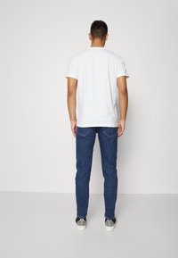 Vit kortärmad t-shirt, blå jeans och svarta sneakers. T-shirten har en klassisk rund halsringning och jeansen har en rak passform.