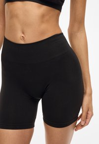Pantalones cortos deportivos negros con una cinturilla alta y acanalada. La tela es suave y elástica, ajustándose ceñidamente alrededor de los muslos y las caderas.