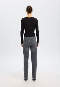 Must Black ribbed long-sleeve top koos hallide sirgete pükstega ja mustade teravate kontsadega, vaadatuna tagant. Lihtne ja minimalistlik disain.
