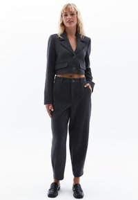 Grijze cropped blazer met twee voorzakken en ronde revers, gecombineerd met bijpassende grijze tapered broek en zwarte instappers.