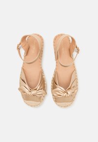 Gold-colored sandals with a knotted bow detail on the front, jute-like textured soles, and adjustable ankle straps.
